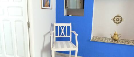 A room with a white door, a white chair, a blue wall, a small window, and a decorative item on a shelf.