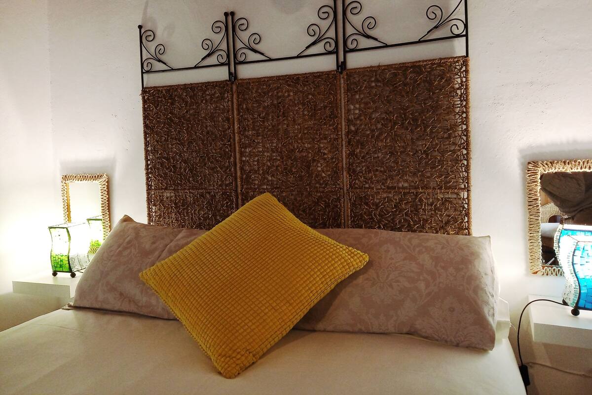 Ein Bett mit Kopfteil, einem gelben Kissen und einem gemusterten Kissen.