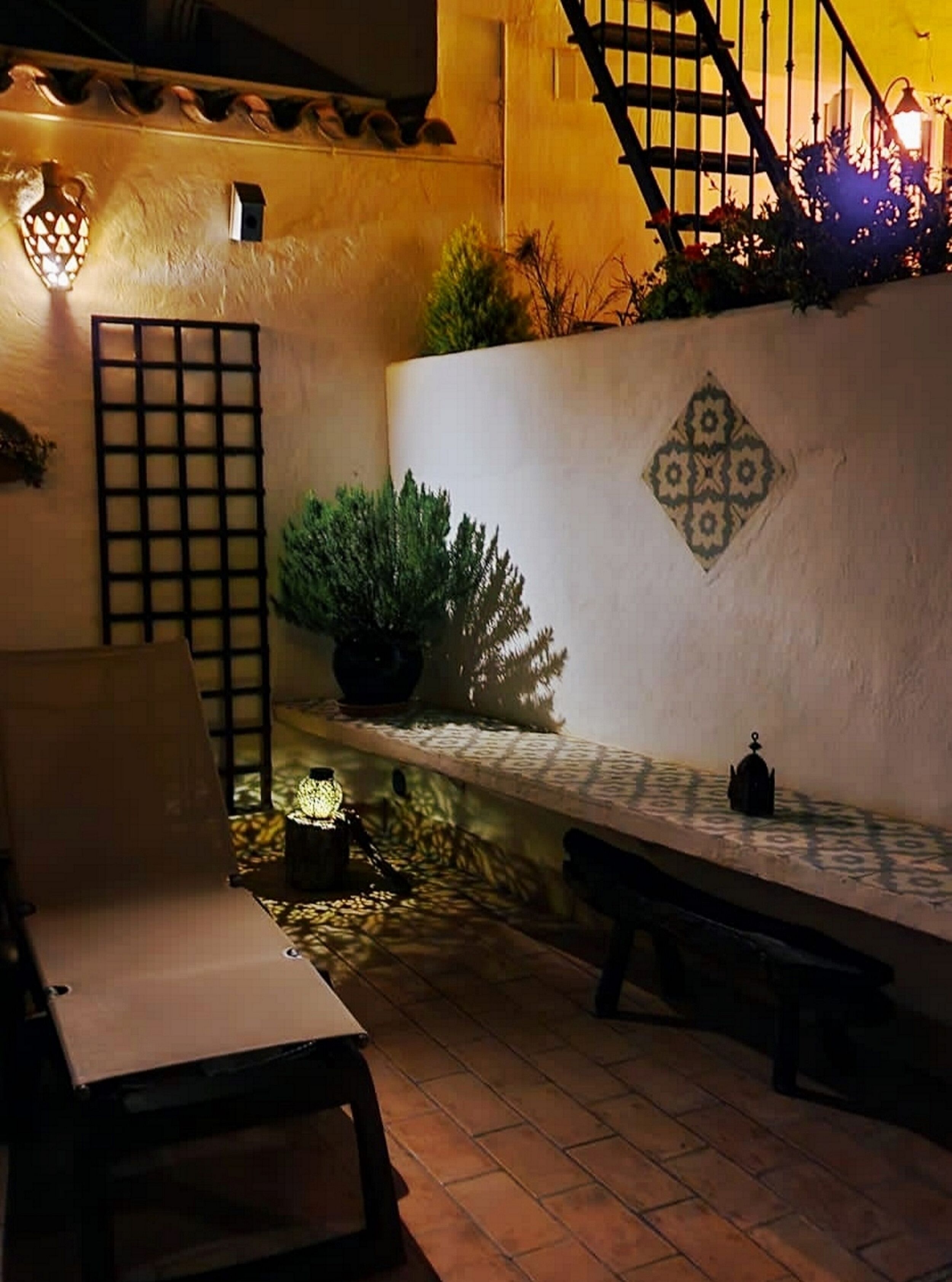 Un rincón al aire libre acogedor, con un banco, una silla, una mesita y una planta en maceta.