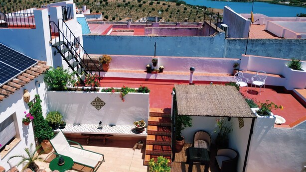 A rooftop terrace with a view of a lake, potted plants, and outdoor seating.