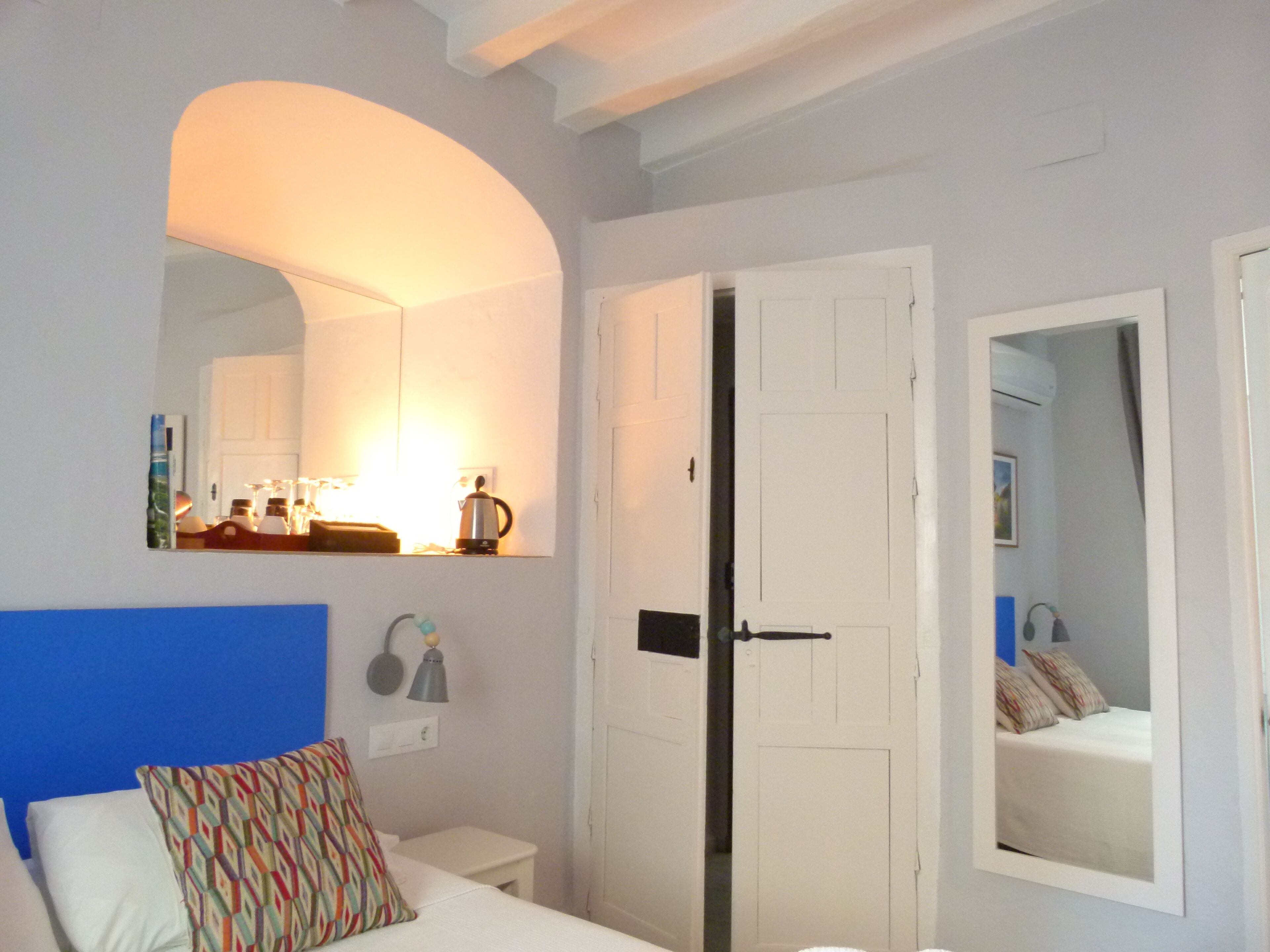 A bedroom with a bed, a nightstand, a mirror, and a door.