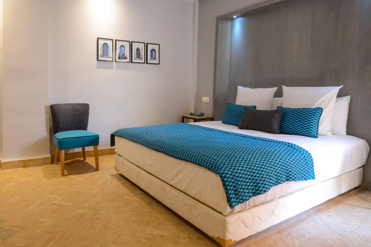 A modern hotel room with a large bed, a chair, and a nightstand.