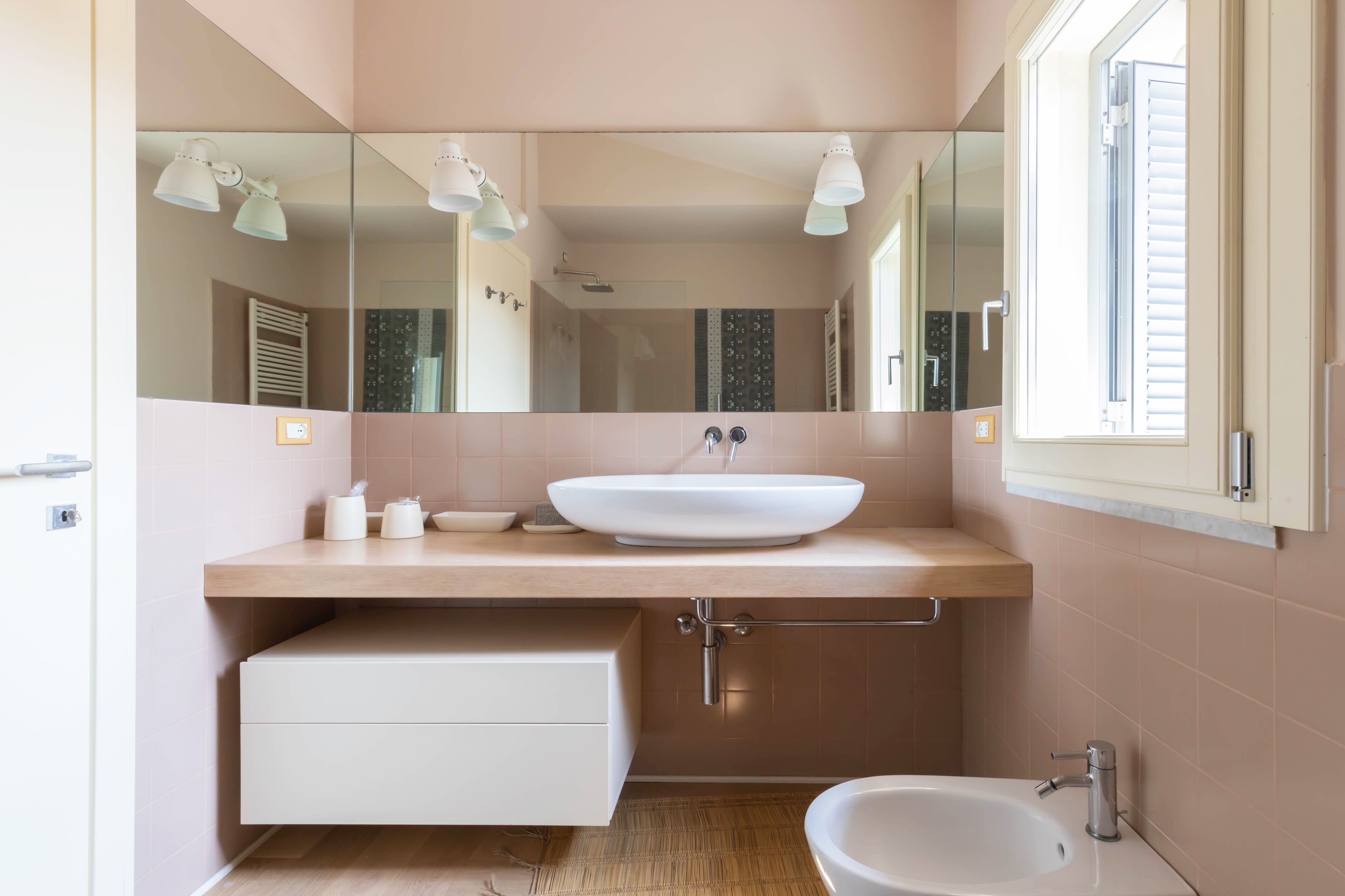 A modern bathroom with a large mirror, a sink, a bidet, and a toilet.