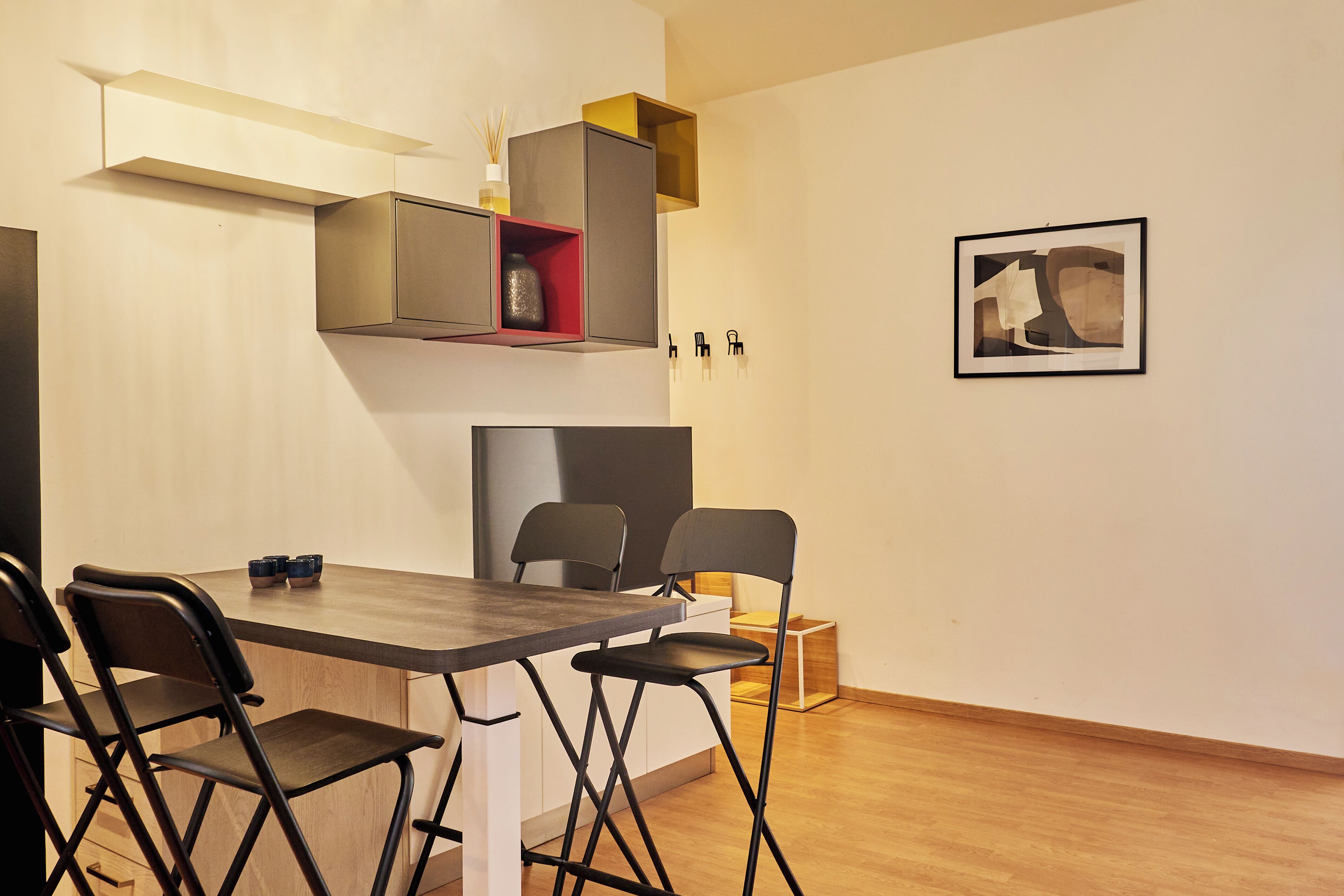 Un espace repas moderne avec une table en bois, des chaises noires et une étagère intégrée agrémentée d’un vase.