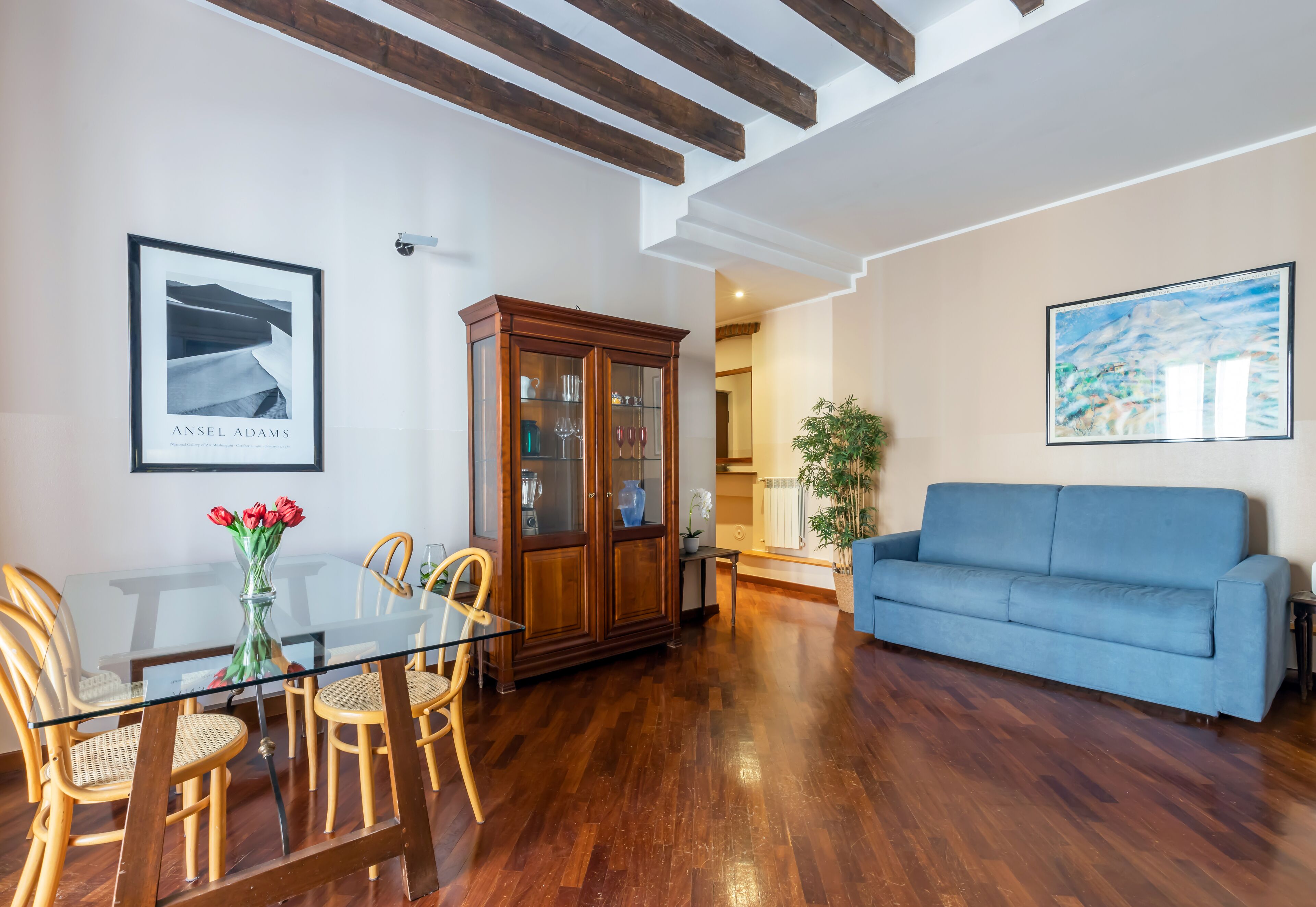 Una sala de estar con una mesa de comedor de cristal, sillas de madera, un sofá azul y un aparador con puertas de vidrio.
