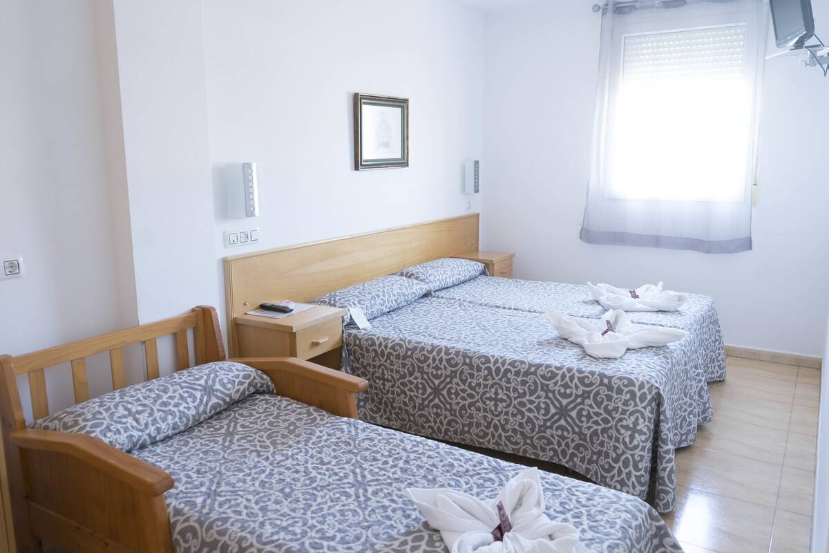 Hotelkamer met twee bedden, een houten hoofdbord, een nachtkastje, een tv aan de muur en een raam met zonwering.