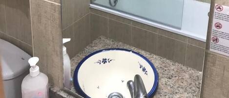Una ducha con paredes de vidrio, una bañera, un lavamanos con borde azul y un dispensador de jabón.