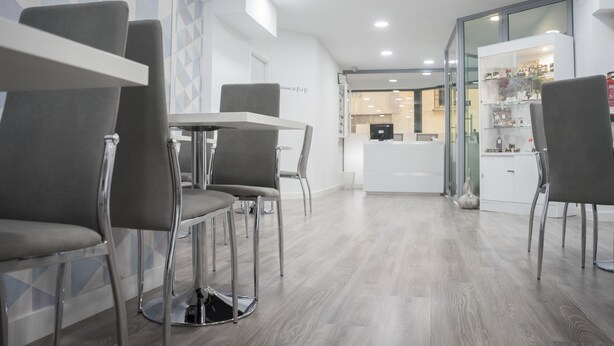 A modern interior with a reception desk, grey upholstered chairs, and a light wood floor.