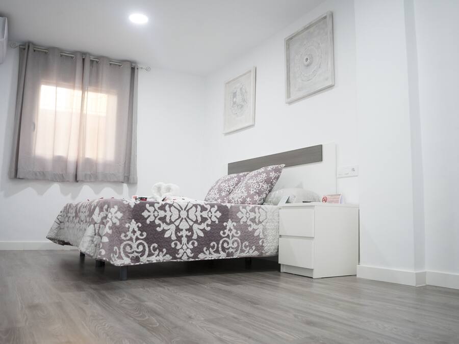 Un dormitorio con cama, mesita de noche y ventana con cortinas.