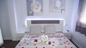 A neatly made bed with a decorative swan and rose petals, a headboard with integrated lighting, and a wall with artistic designs.