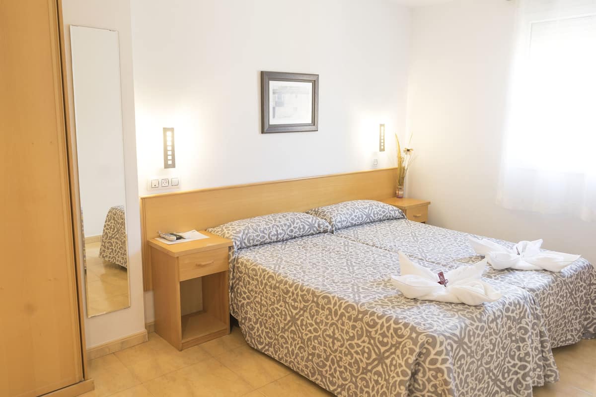 Een hotelkamer met een bed, nachtkastje, spiegel en een foto in een lijst aan de muur.