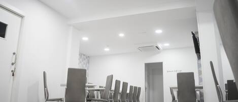 Uma sala de conferências moderna com uma mesa comprida e várias cadeiras, paredes brancas e piso de madeira.
