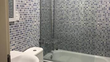 Een badkamer met een douchecabine van glas, een wit toilet en een bad.