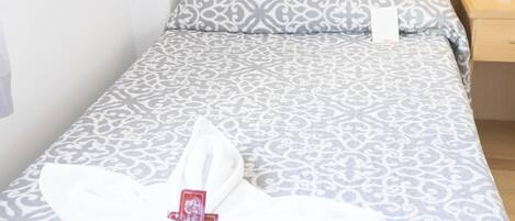 A neatly made bed with a patterned bedspread and a towel folded in a decorative shape on the bed.