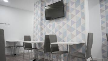 A conference room with a flat-screen TV mounted on the wall, grey chairs, and white tables.