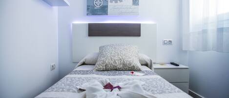 A neatly made bed with patterned bedding, a bedside table with a remote control, and a wall-mounted decorative piece above the bed.