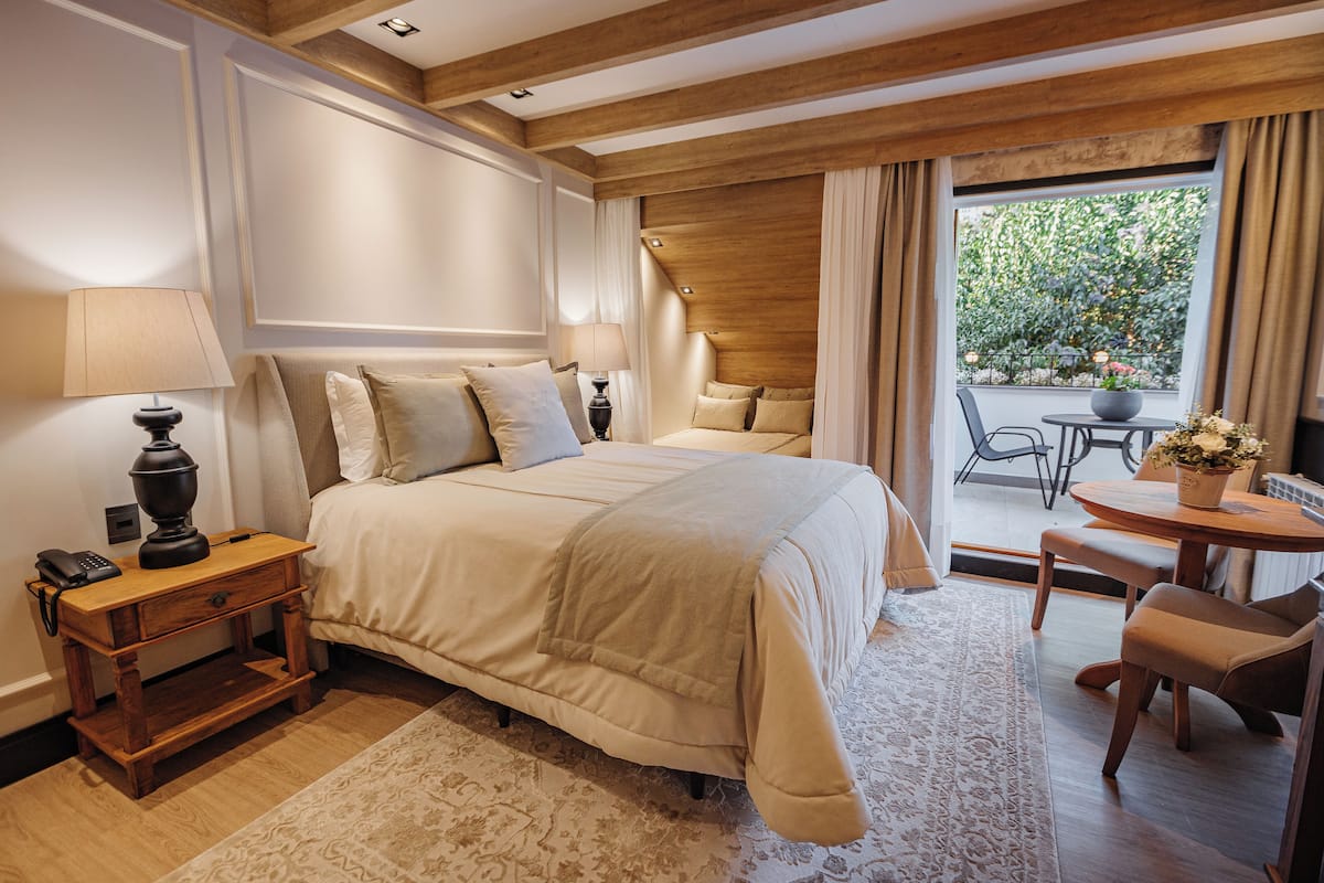 A bedroom with a large bed, bedside tables, a small table with a plant, and a view of the outdoors.
