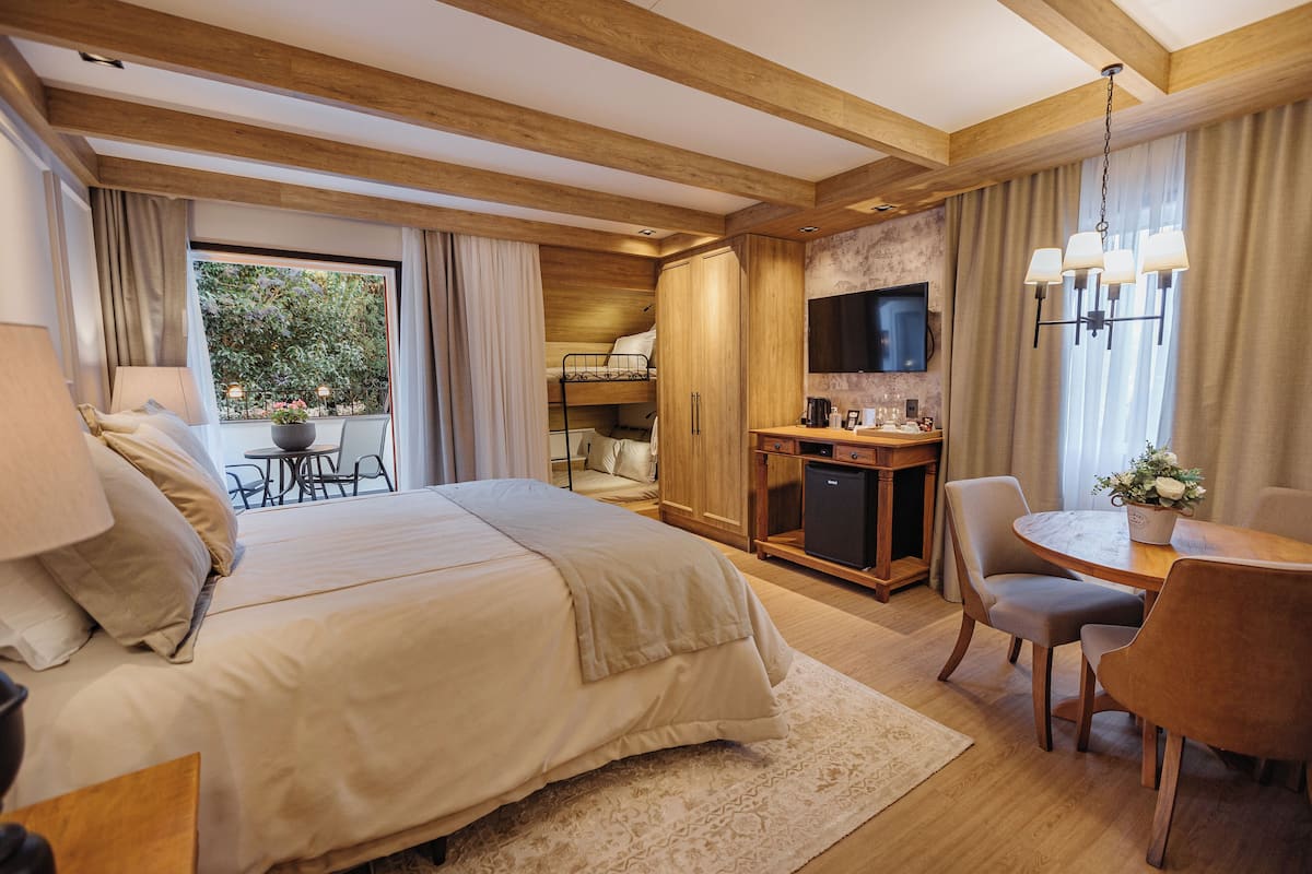 A bedroom with a large bed, a desk with a chair, a television, and a window with curtains.