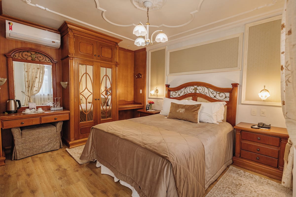 A bedroom with a large bed, wooden wardrobe, dresser, and a vanity with a mirror.