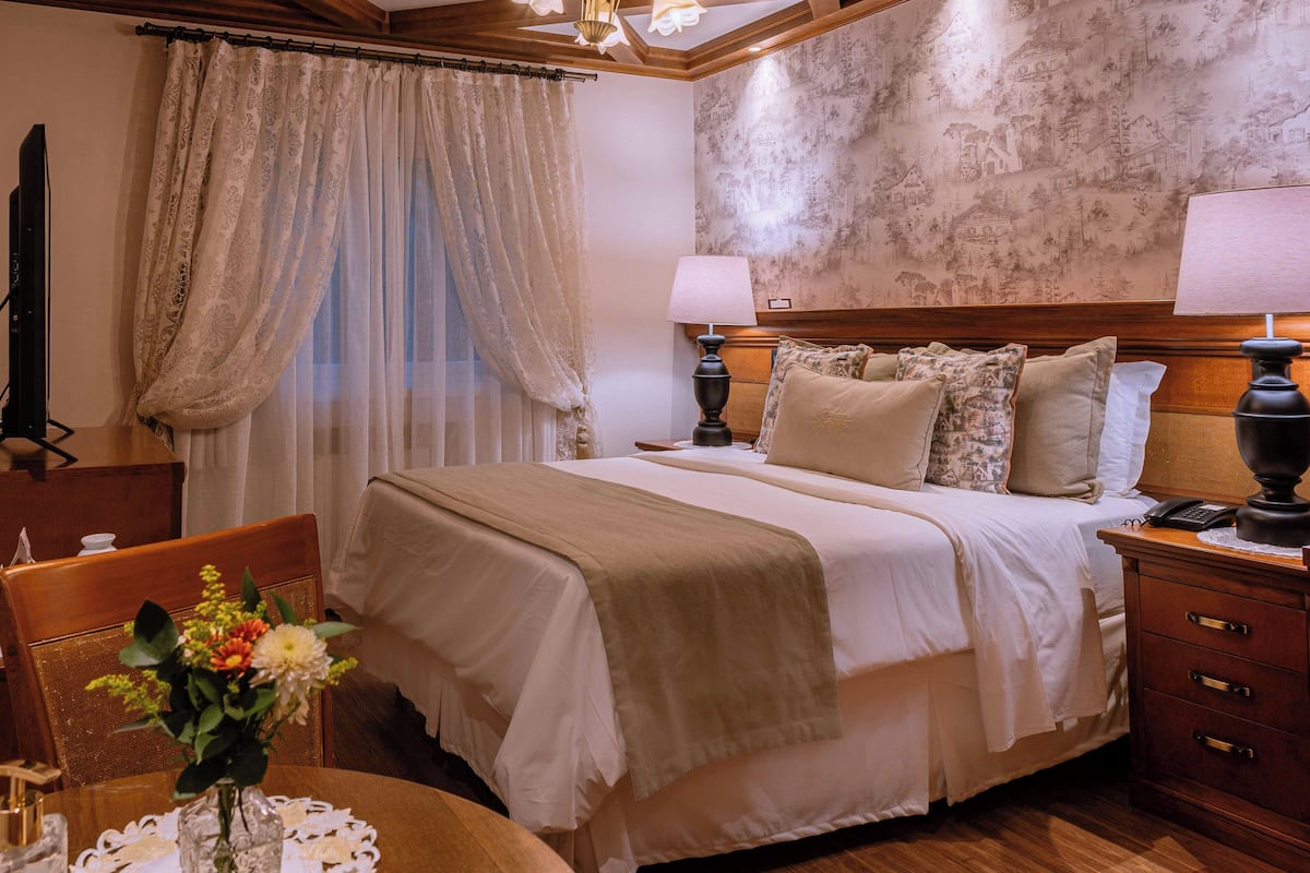 A hotel room with a large bed, two bedside tables, a desk with a chair, and a decorative vase on the desk.