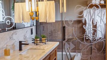 Un baño moderno con tocador de mármol, cabina de ducha con vidrio y tozaletas con toallas blancas.