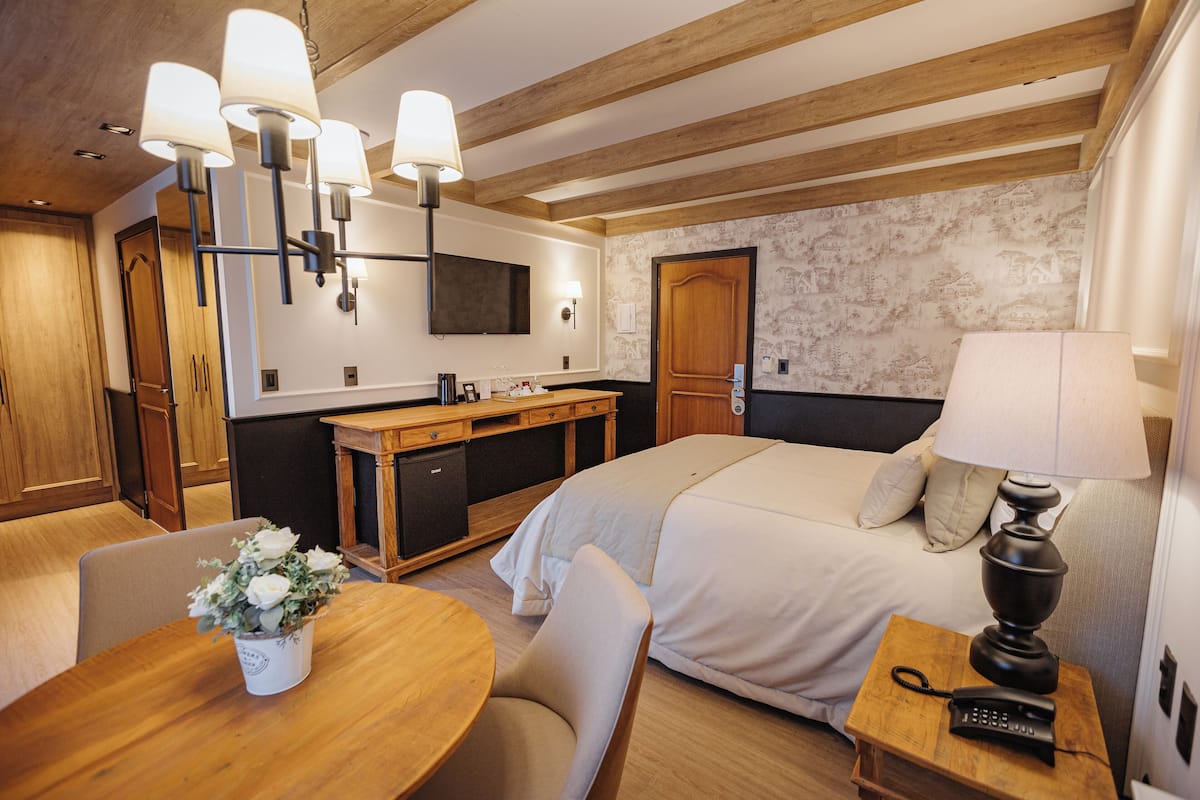 A hotel room with a bed, bedside table, lamp, desk, chair, and a small table with a vase of flowers.