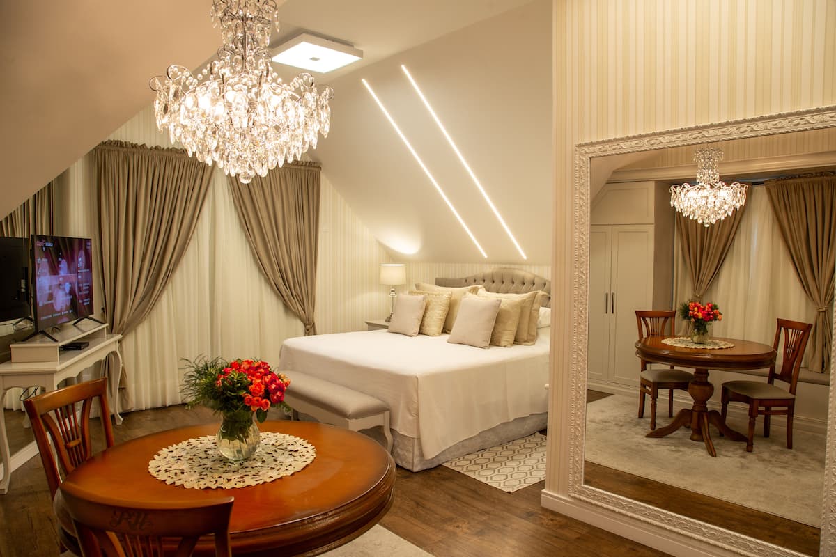 A hotel room with a large bed, a sitting area with a table and chairs, a television, and a large mirror.