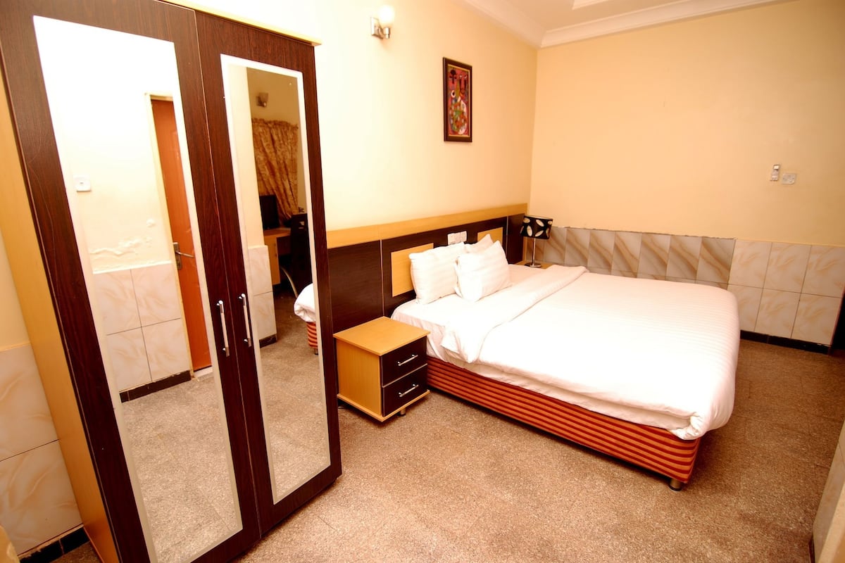 Quarto de hotel com cama, mesa de cabeceira, guarda-roupa e espelho.