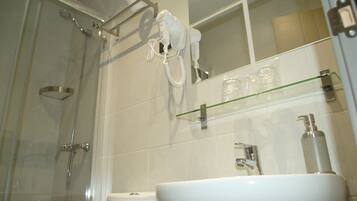 Un baño con cabina de ducha de vidrio, un lavabo blanco y un secador de pelo montado en la pared.