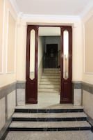 A set of marble stairs leading to a dark wooden door with glass panels, flanked by cream-colored walls and a marble base.