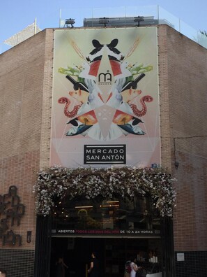 A building with a large mural advertising 'Mercado San Anton' and a sign indicating it's open all year. - Fuencarral Rooms (Madrid)