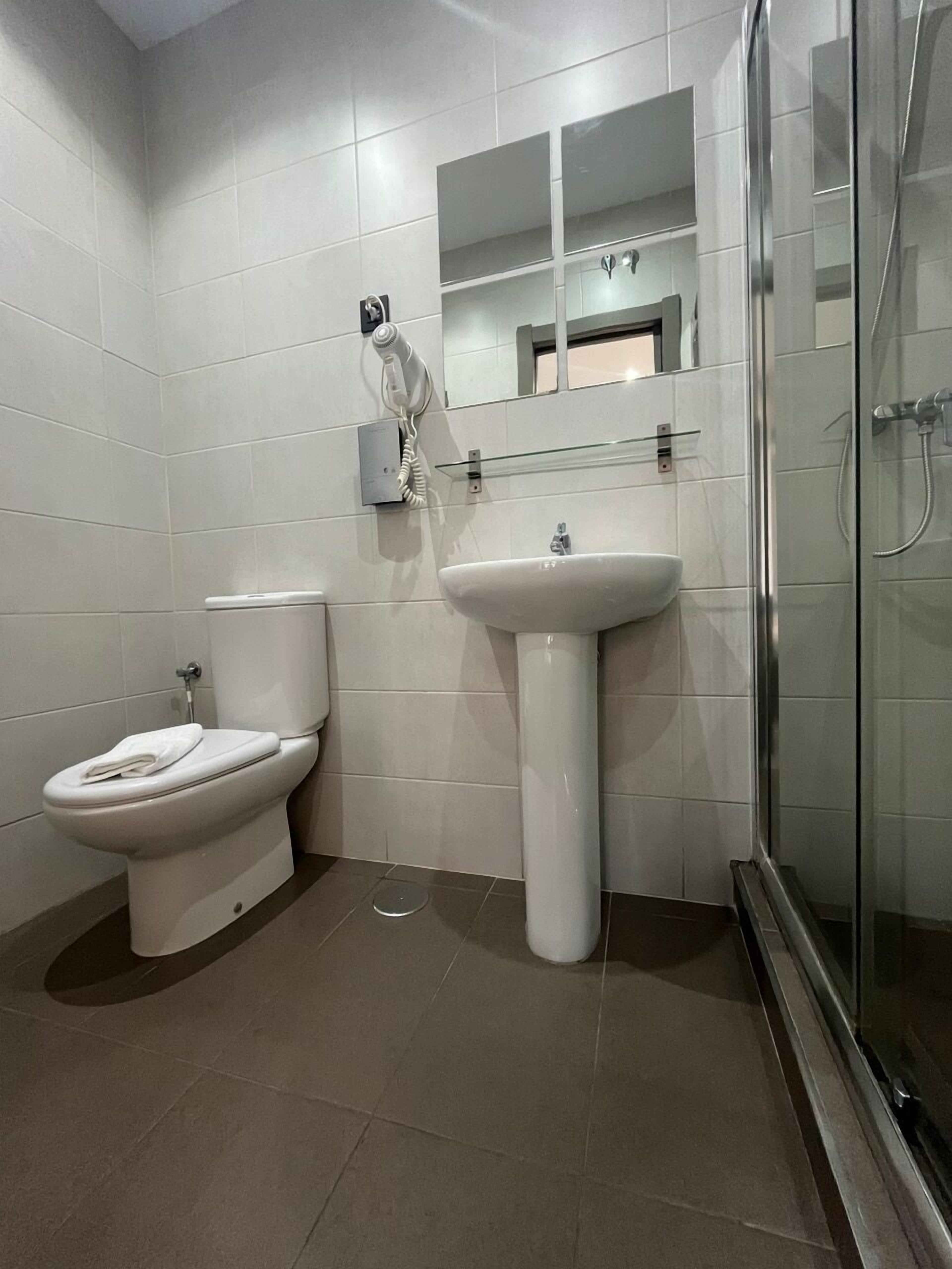 A bathroom with a toilet, a pedestal sink, and a glass-enclosed shower.