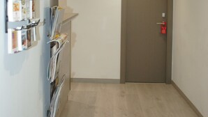 Un pasillo con una puerta marcada con el número 33, un equipo de aire acondicionado arriba y un estante en la pared con revistas.