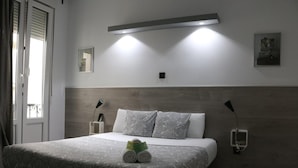 Una habitación de hotel moderna con una cama grande, dos lámparas de noche, una luz en la pared y un pequeño cuadro colgado.
