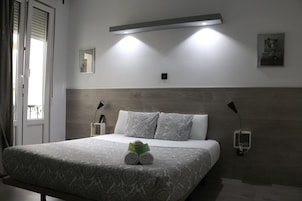 Una camera d'albergo moderna con un letto grande, due lampade ai comodini, una luce a parete e un piccolo quadro appeso.