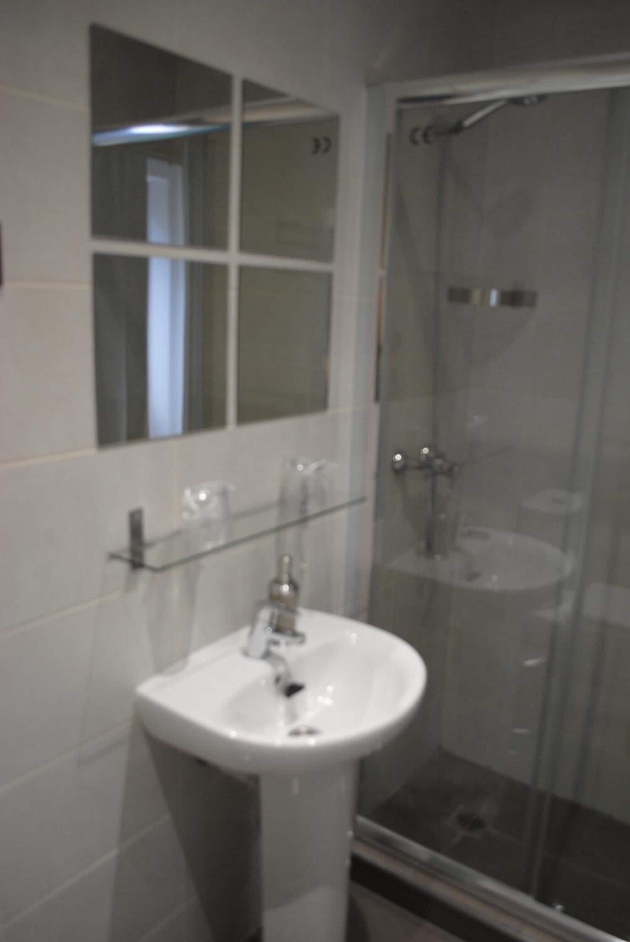 A bathroom with a glass shower enclosure, a white sink, and a mirror above the sink.