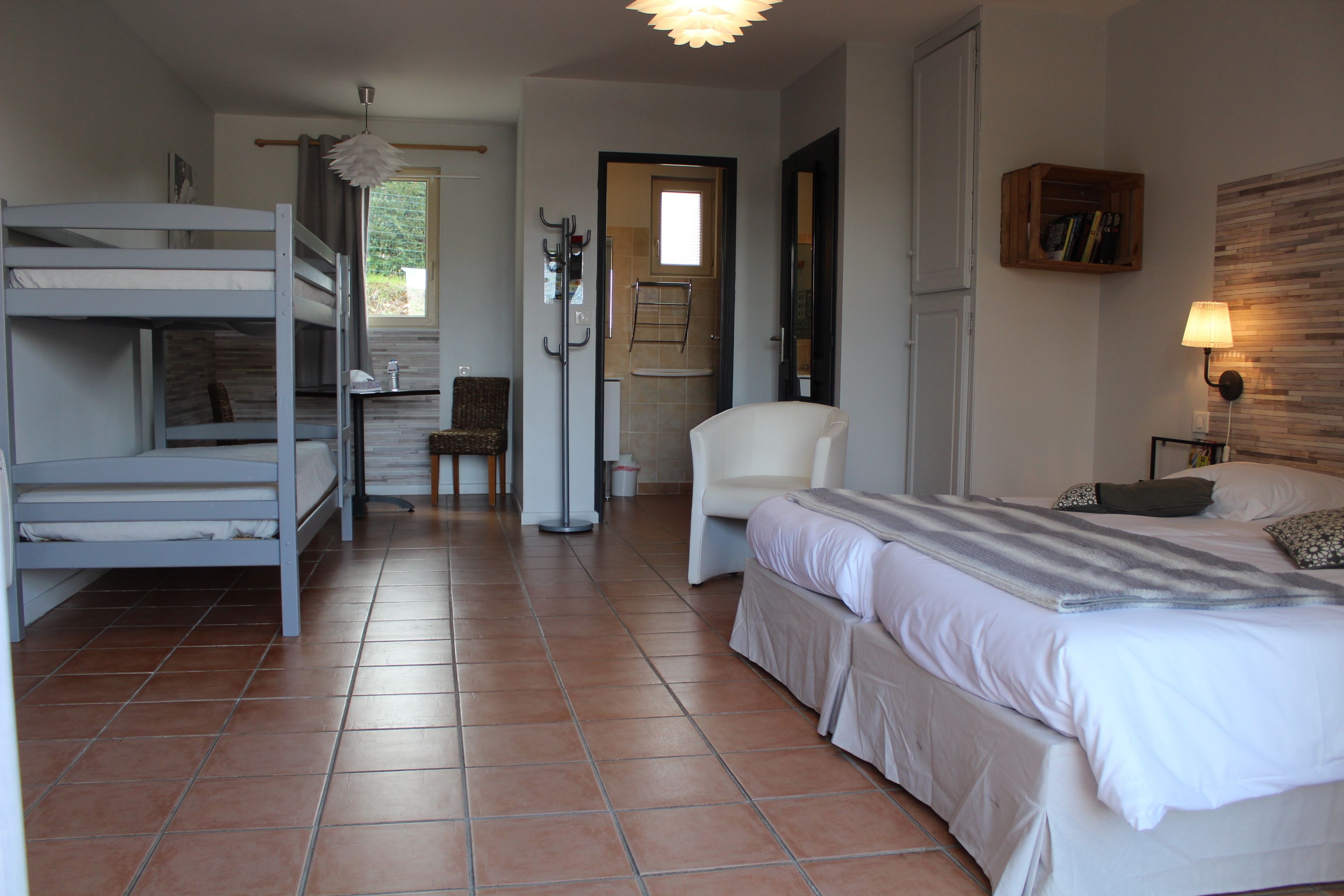 Un dormitorio con literas, una silla, un escritorio y una cama con lámpara.