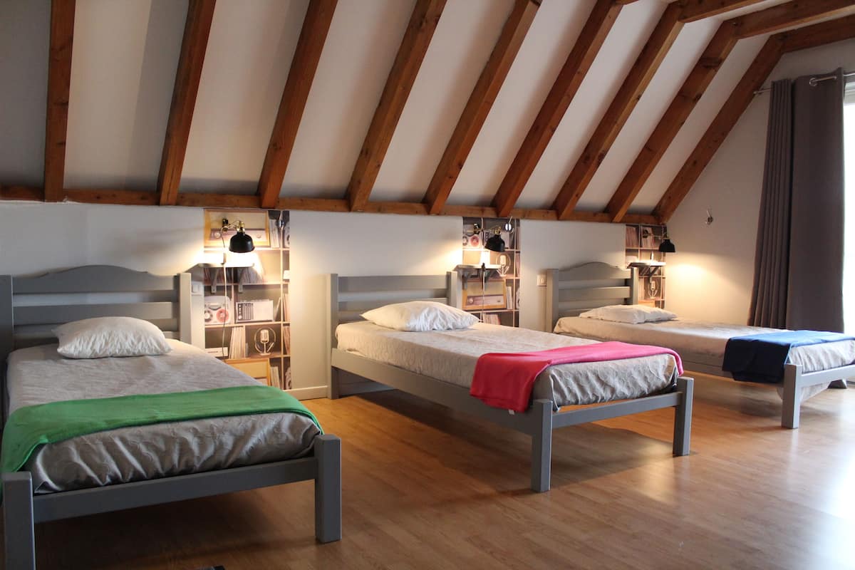 A room with three single beds, wooden beams on the ceiling, and bedside tables with lamps.