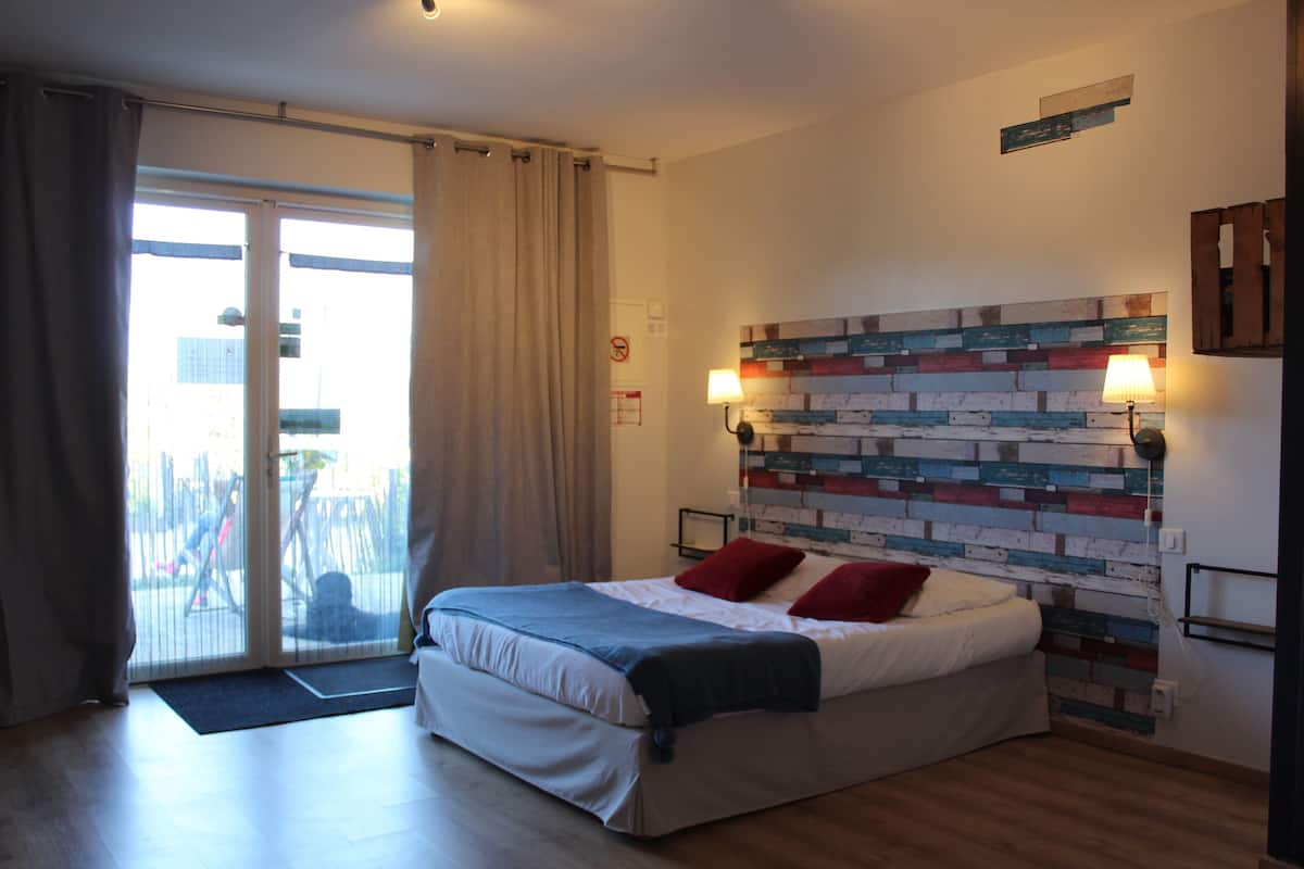A bedroom with a bed, a view through a sliding door, a brick-patterned headboard, and a lamp on the wall.