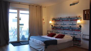 Une chambre avec un lit, une vue à travers une porte coulissante, une tête de lit décorée d’un motif en briques et une lampe fixée au mur.