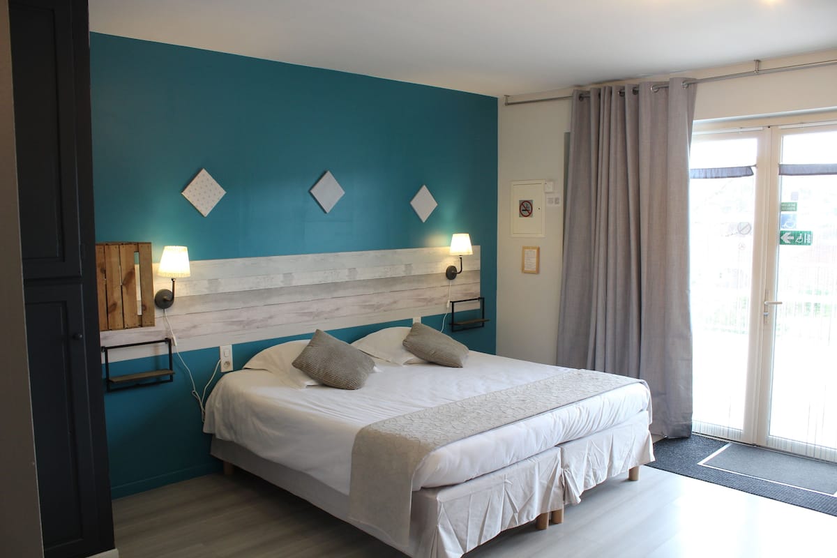 A bedroom with a bed, two bedside lamps, a headboard, and a view of the outside through a window with curtains.