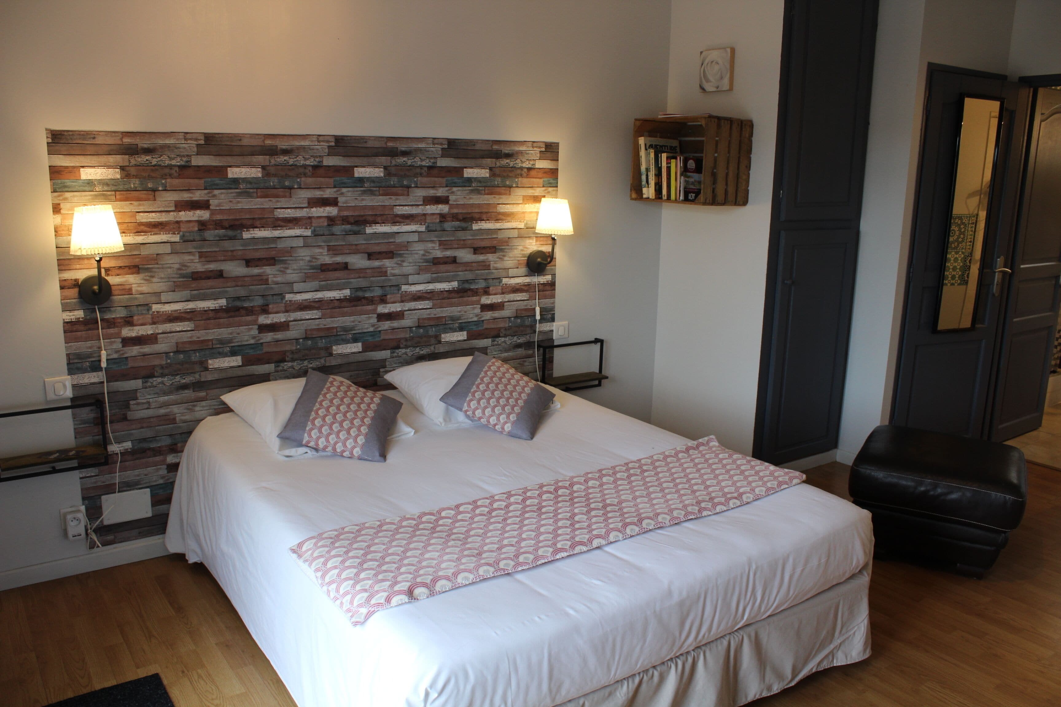 Een opgemaakt bed met een beddegoed met patroon, twee bedlampen en een houten hoofdbord.