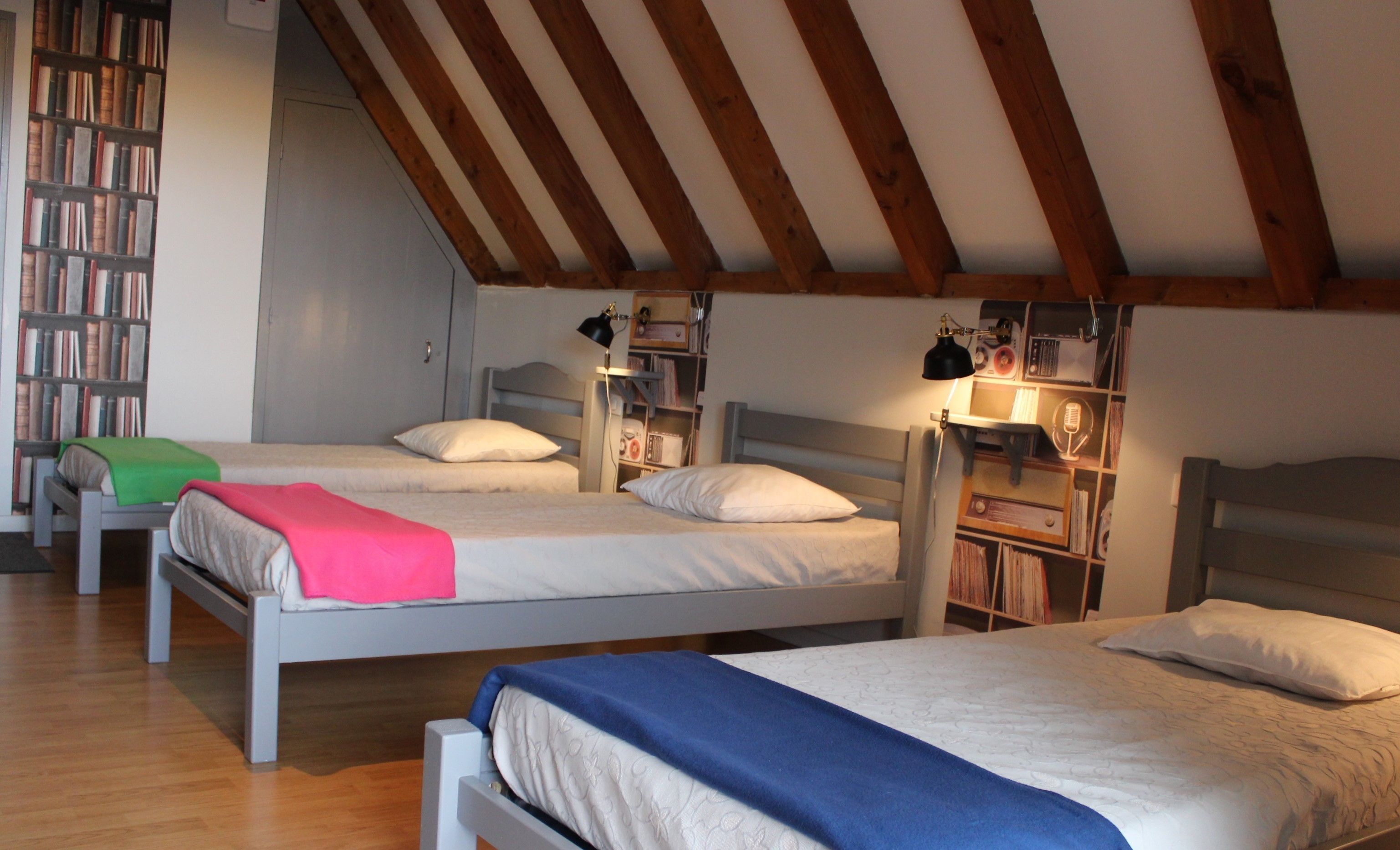 A cozy attic bedroom with two beds, a bookshelf, and a radio collection.