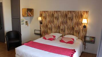 Een net opgemaakt bed met witte beddengoed en rode accenten, een houten hoofdbord, twee bedlampjes, een zwarte stoel en een klein plankje met boeken.