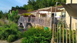 Un espacio al aire libre cubierto con una escalera que lleva a un balcón, rodeado de vegetación y un edificio al fondo.