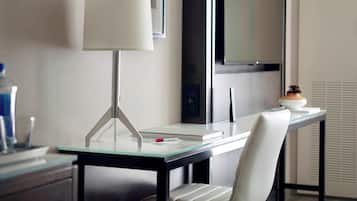 A modern hotel room with a glass desk, a white chair, a lamp, and a television.