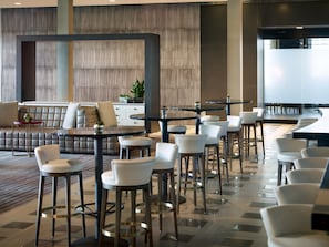 A modern lounge area with a sofa, bar stools, and a dining area with tables and chairs. - Marriott Columbus OSU (Columbus)