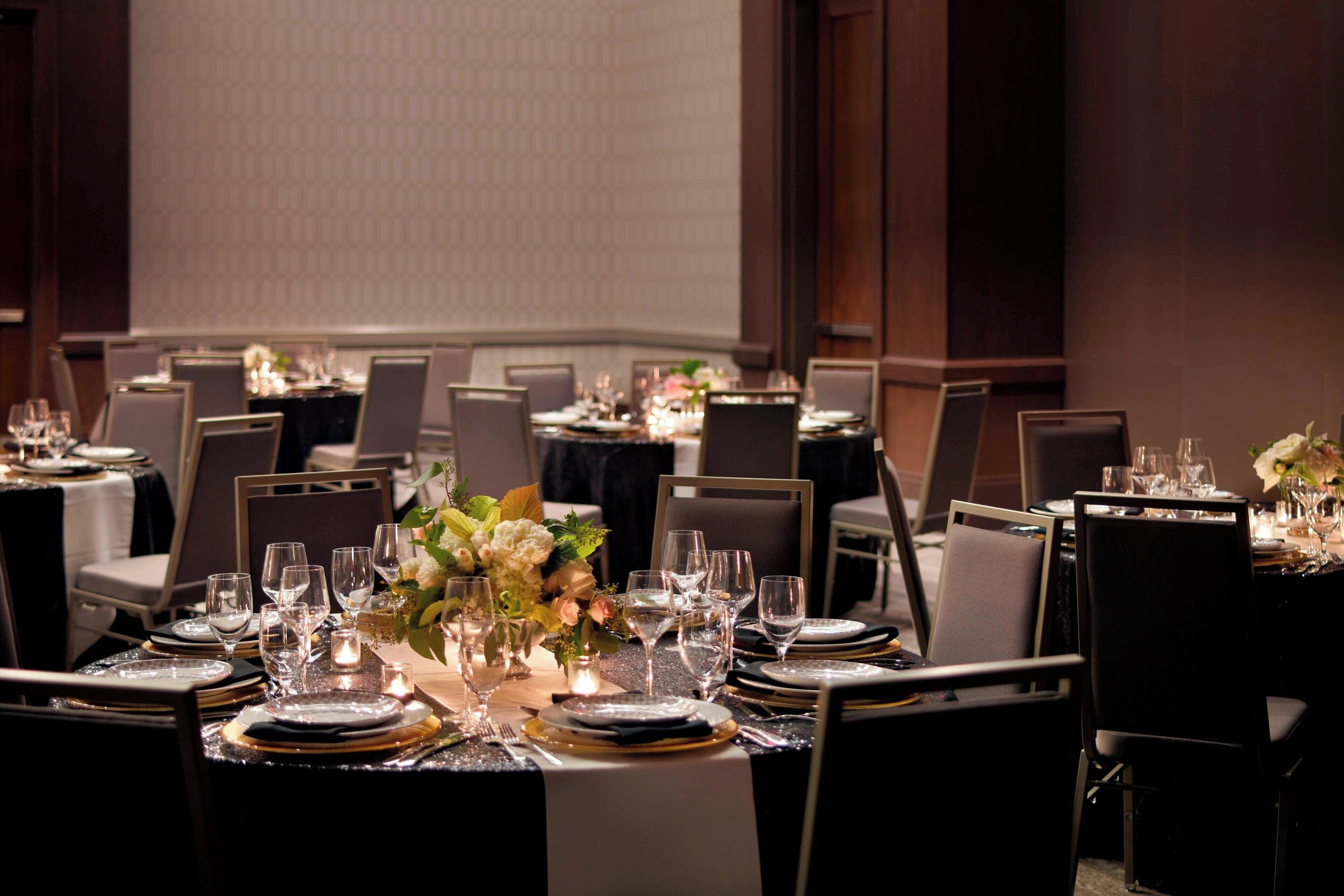 A banquet hall with round tables set for dining, each with place settings, glasses, and floral centerpieces.