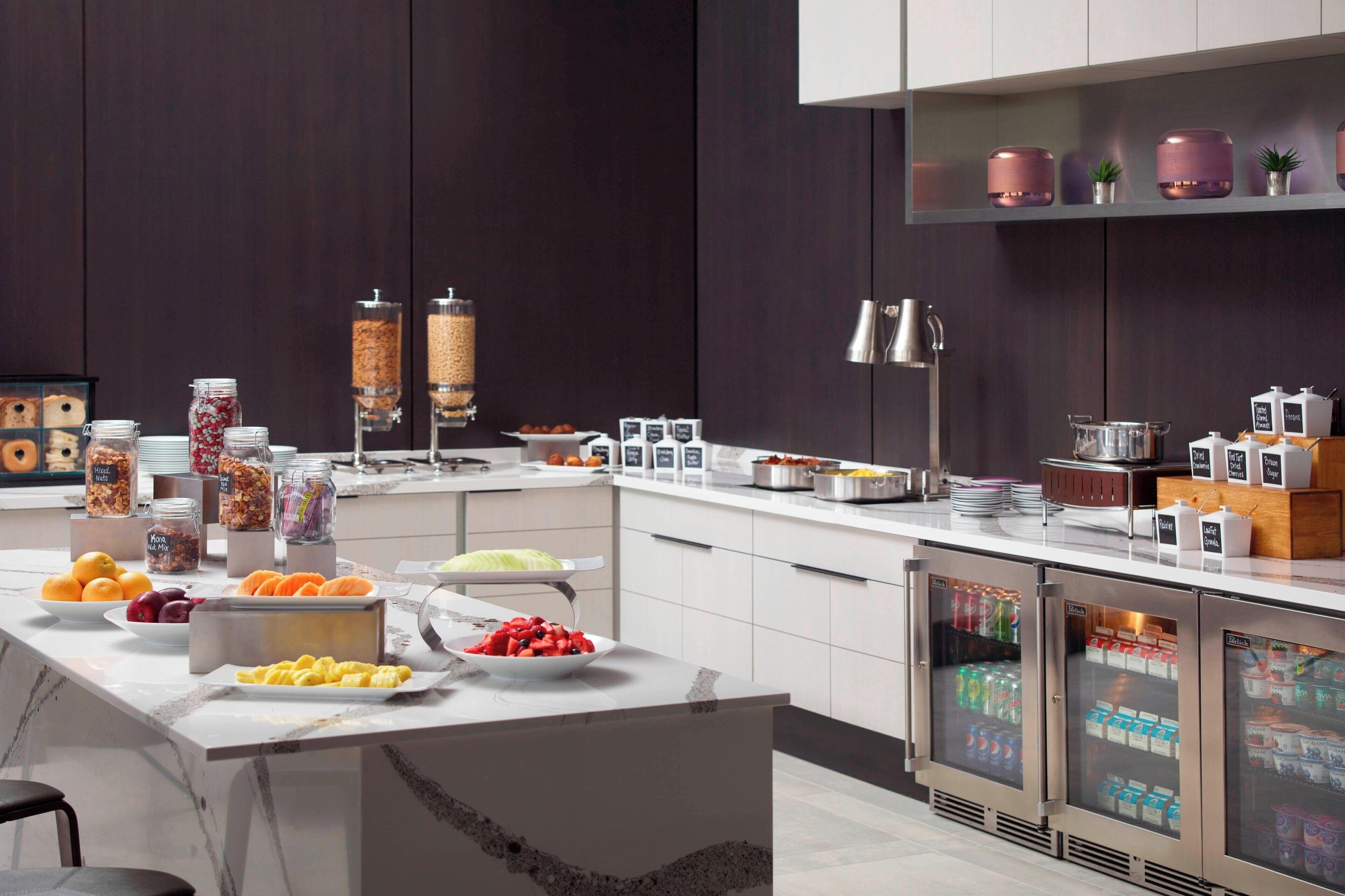 A modern breakfast bar with a variety of food and drink options, including fruits, cereals, and beverages.