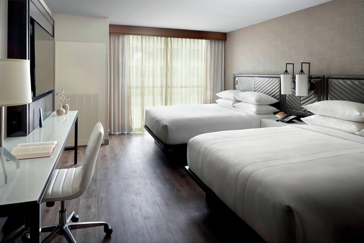 Una habitación de hotel con dos camas, un escritorio con silla, televisión y ventana con cortinas.